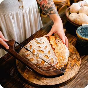 Hands slicing a freshly baked loaf of sourdough bread