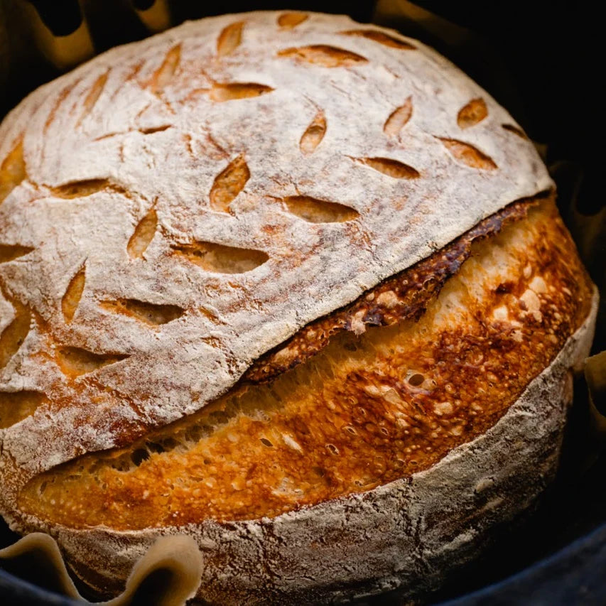 Loaf of bread with a rustic crust and scored top, set against a dark background.
