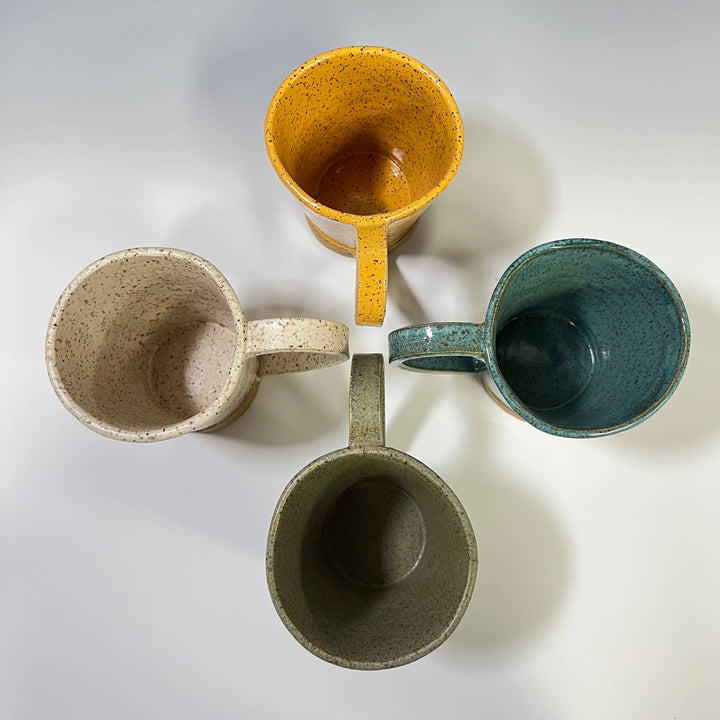Four ceramic mugs in different colors on a light gray background