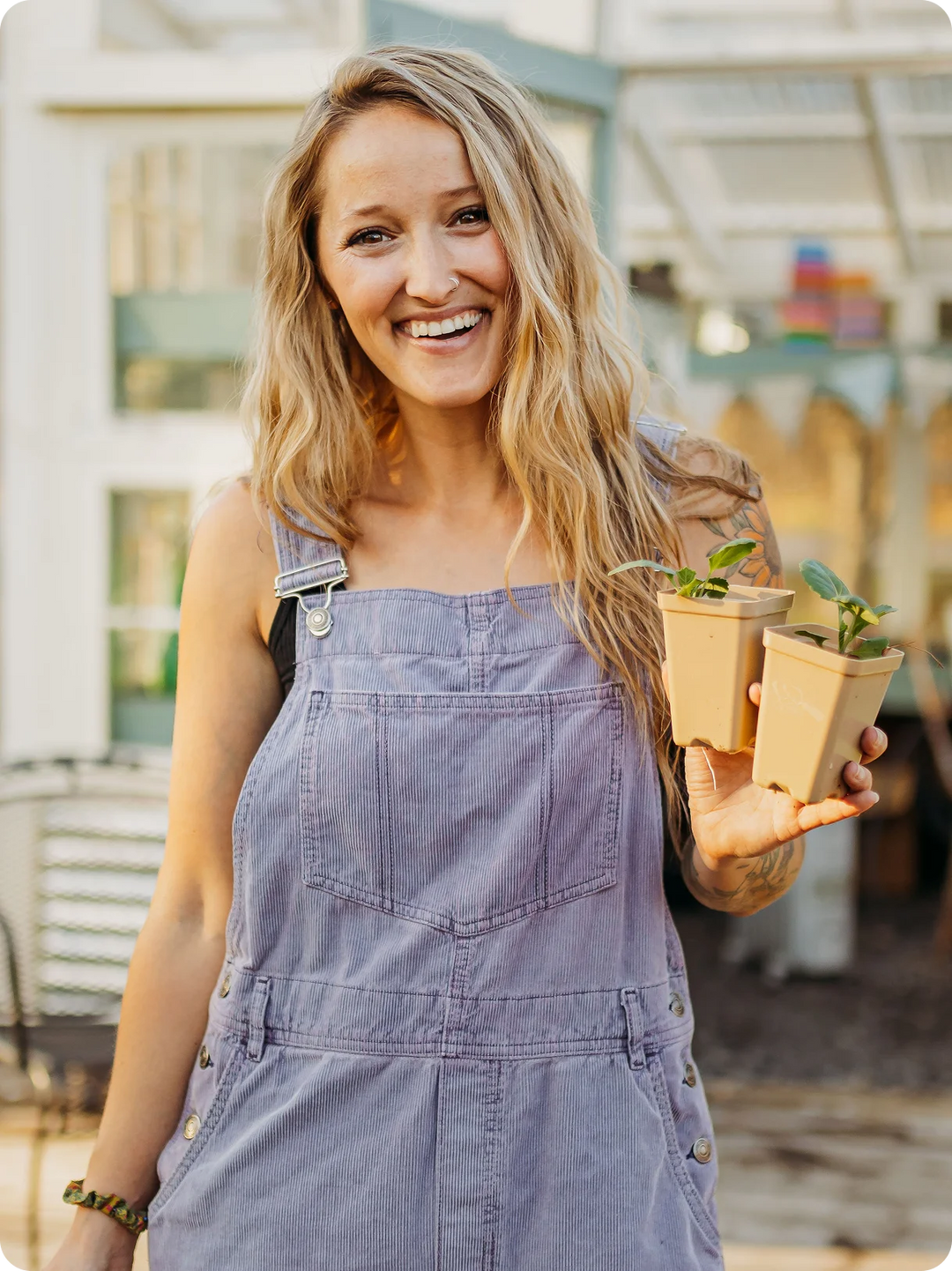 Jill in a denim overalls holding small plants in a greenhouse