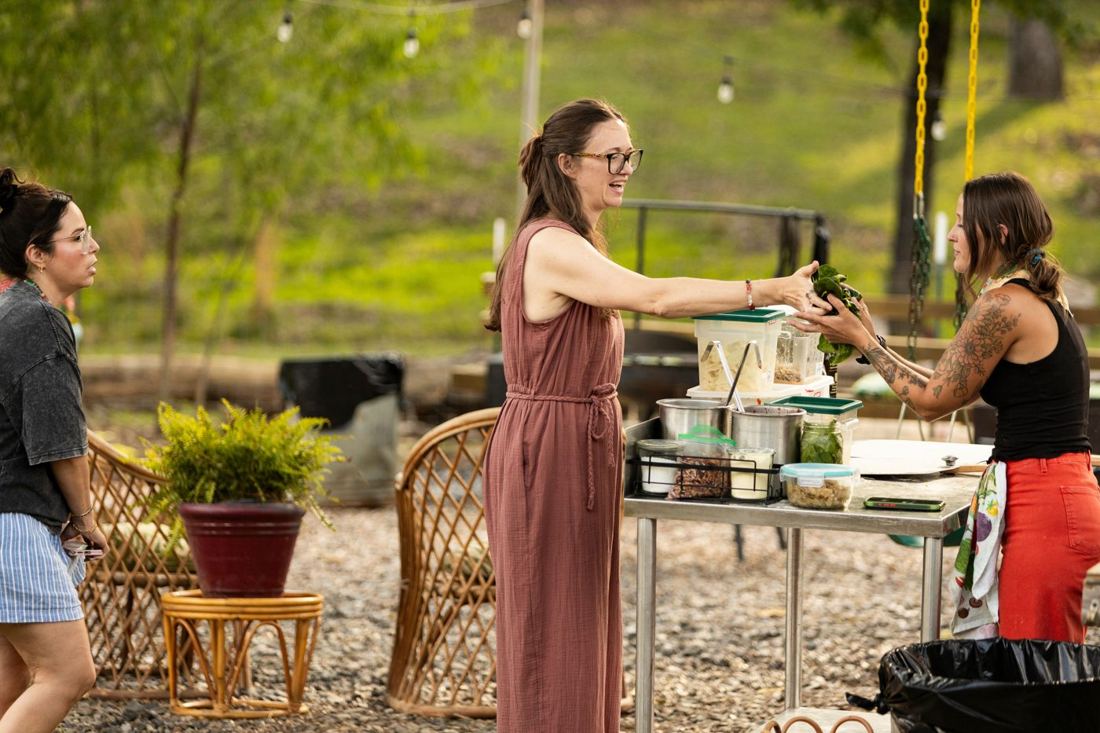 A guest handing a bunch of fresh spinach across the prep table to Jill