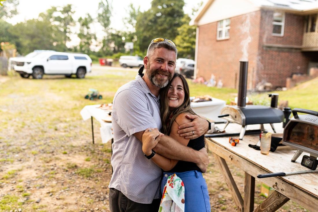 A couple hugging and smiling beside the pizza ovens