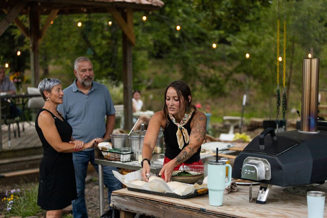 Jill shaping dough at the prep station while two guests watch under the string lights