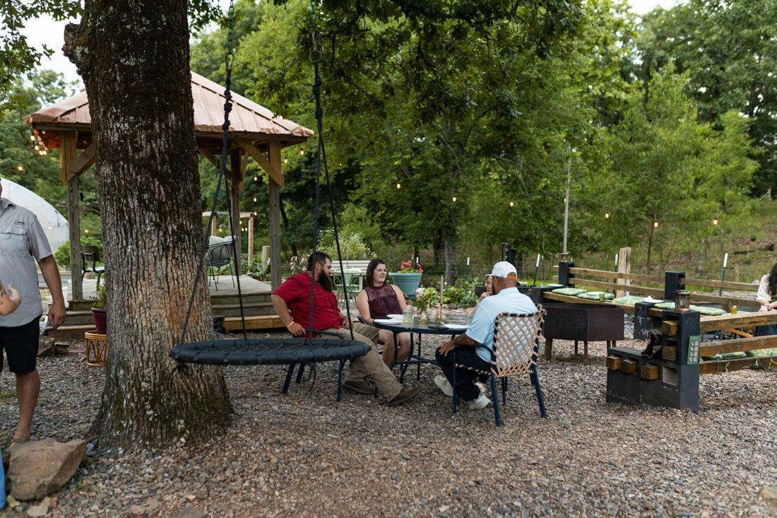 A group of four chatting at a small table under a big oak tree near the pavilion