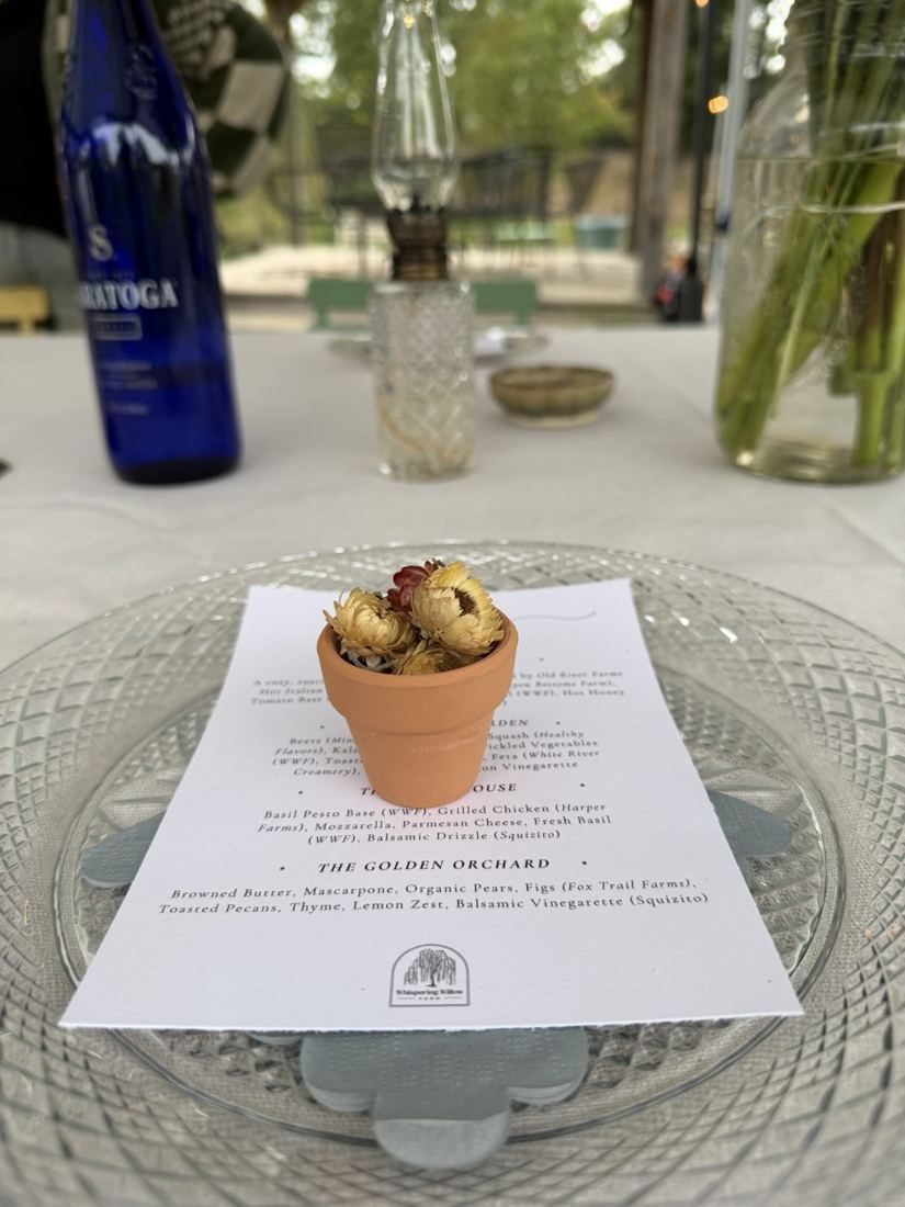 A printed pizza night menu on a cut-glass plate with a tiny terracotta pot of dried strawflowers