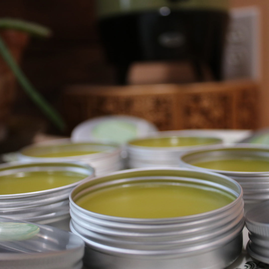 Multiple open tins containing yellow-green herbal balm or salve arranged on a surface.