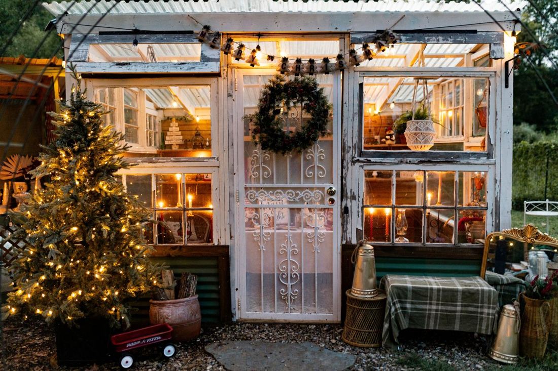 The greenhouse front dressed for Christmas with a Merry Christmas banner, wreath, lit tree and red wagon
