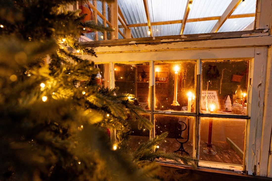 Candles glowing in the old greenhouse windows, the Merry and Bright table visible inside