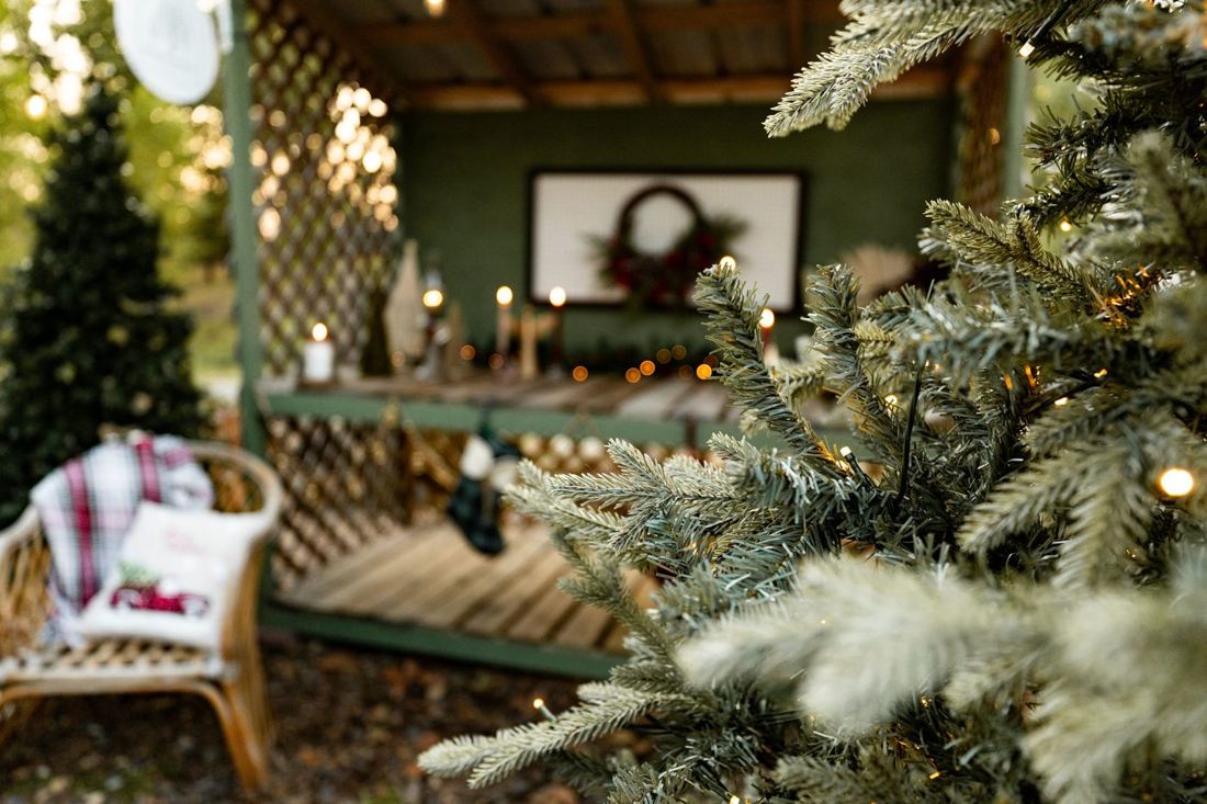 A snowy-tipped tree branch with the candlelit potting bench and a cozy chair behind