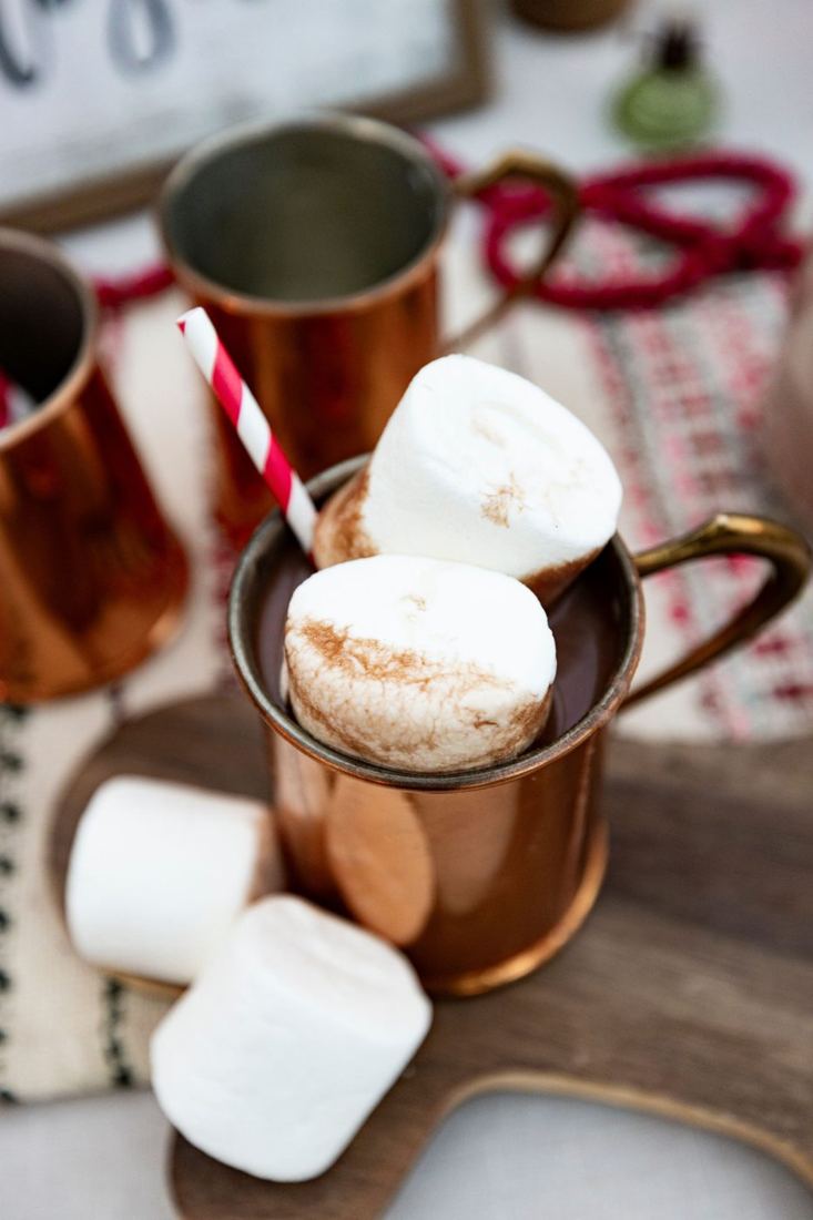 A copper mug of hot cocoa topped with giant marshmallows and a striped straw